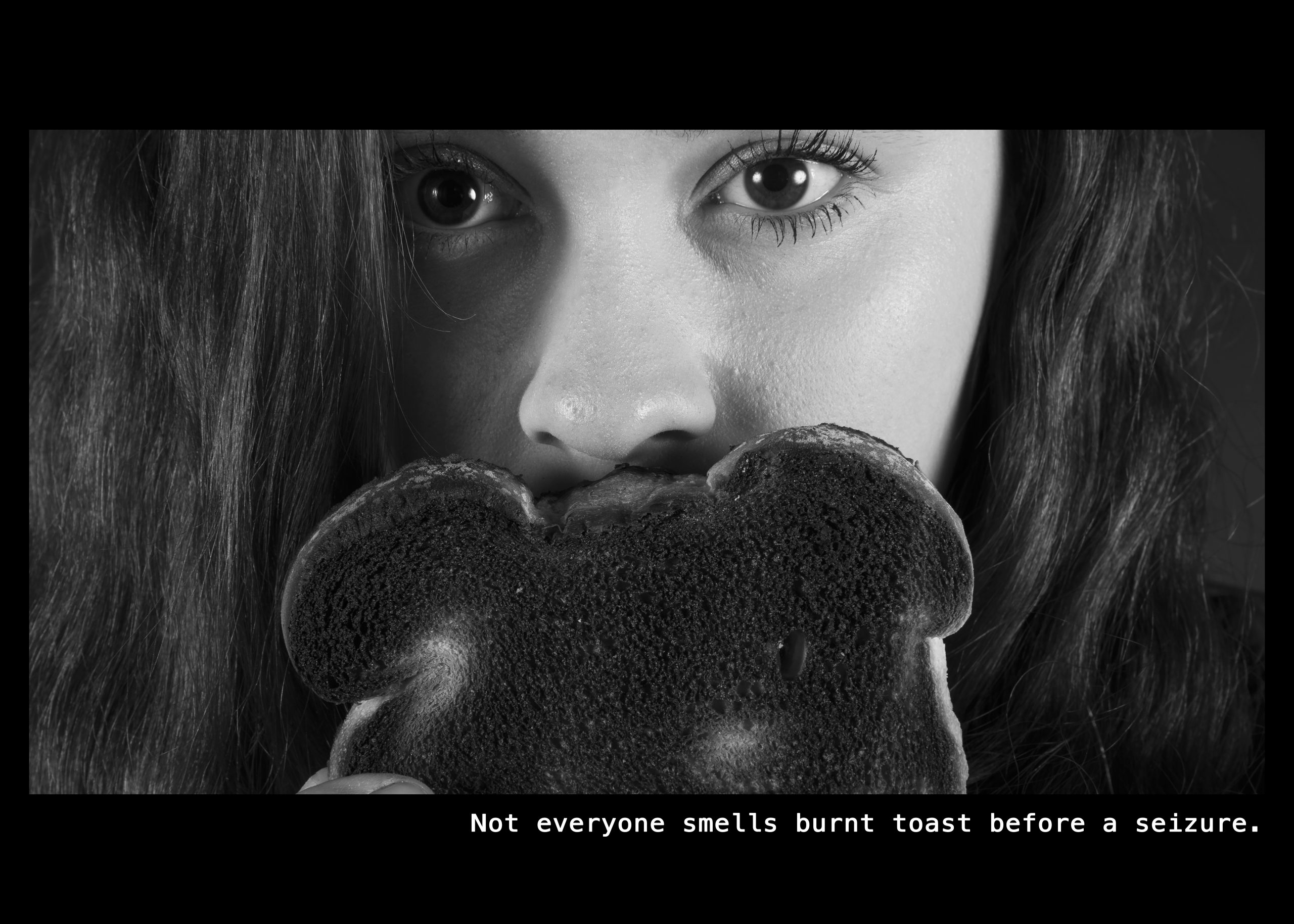 Image of a woman with a piece of burnt toast covering the lower half of her face. Text: Not everyone smells burnt toast before a seizure.