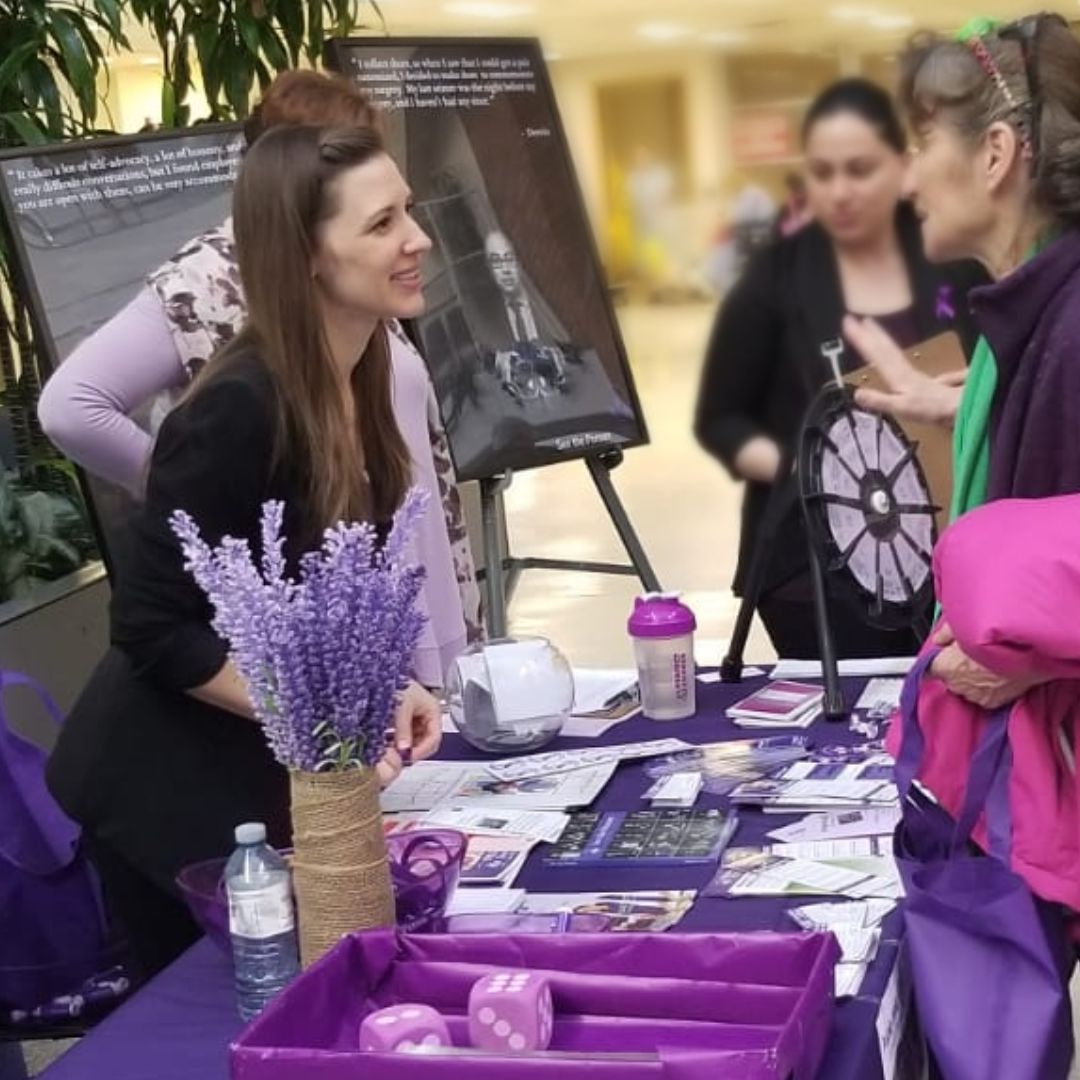 A woman leans over a table full of brochures to speak with another woman