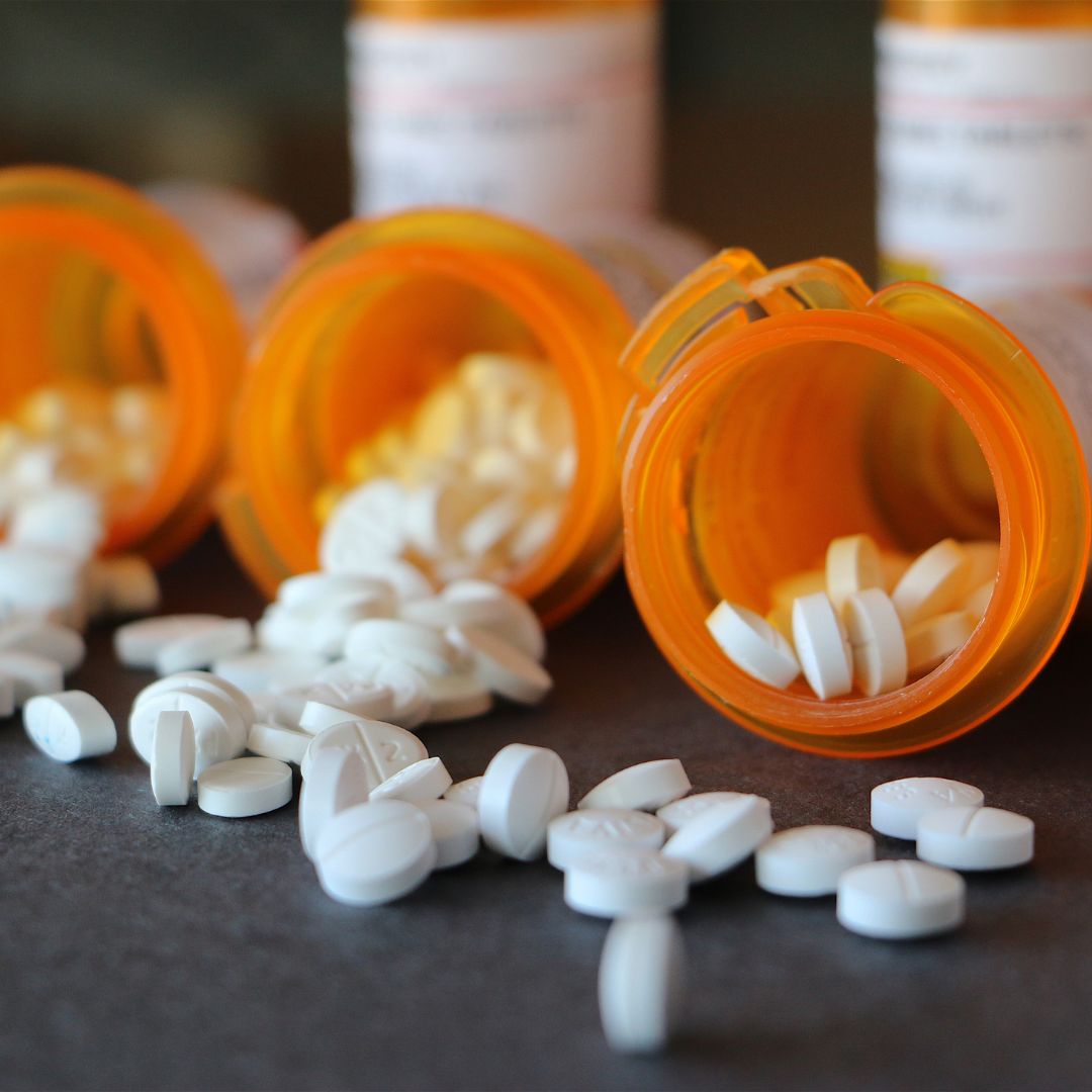 Multiple orange pill bottles, some tipped on their side with white pills spilling out.