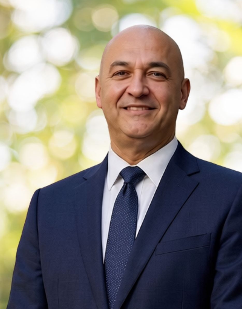 Mid range photo of Wassim Adly, wearing a blue suit and tie, smiling at the camera.